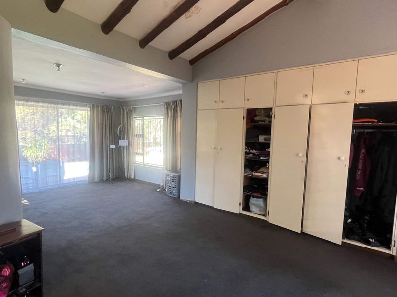 Spacious bedroom featuring exposed timber ceiling beams, extensive built-in cupboard storage, and direct access to the outdoor area via sliding glass doors.