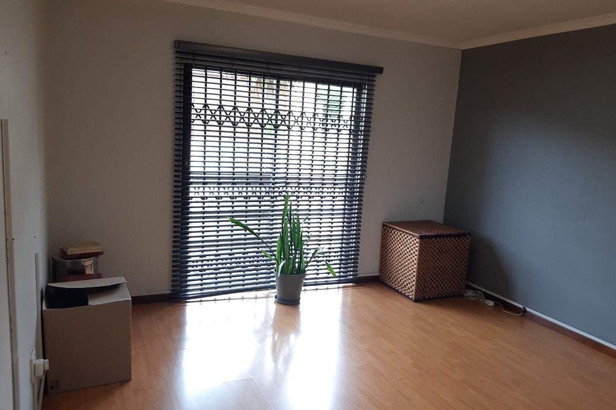 A bright living room featuring laminate wood flooring, a dark grey feature wall, and a large window fitted with a security gate and blinds.
