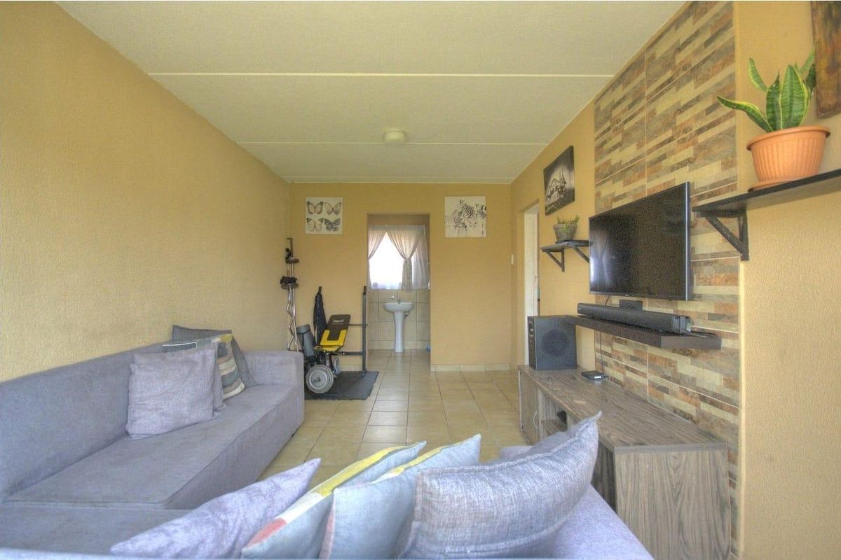 A living room featuring tiled flooring and a stone-cladding feature wall, with an adjacent area containing a pedestal basin.