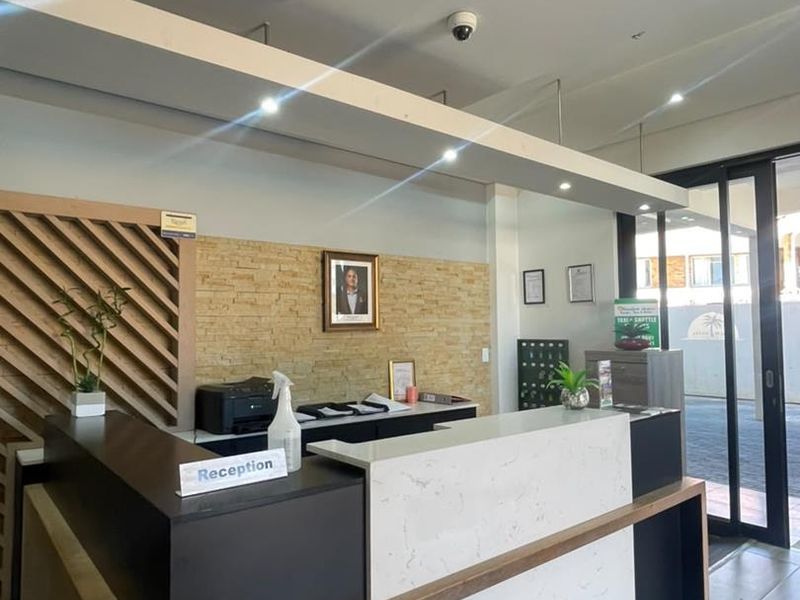 A professional reception area featuring a modern built-in desk, stone accent wall, ceiling-mounted air conditioning, and tiled flooring with glass entry doors.