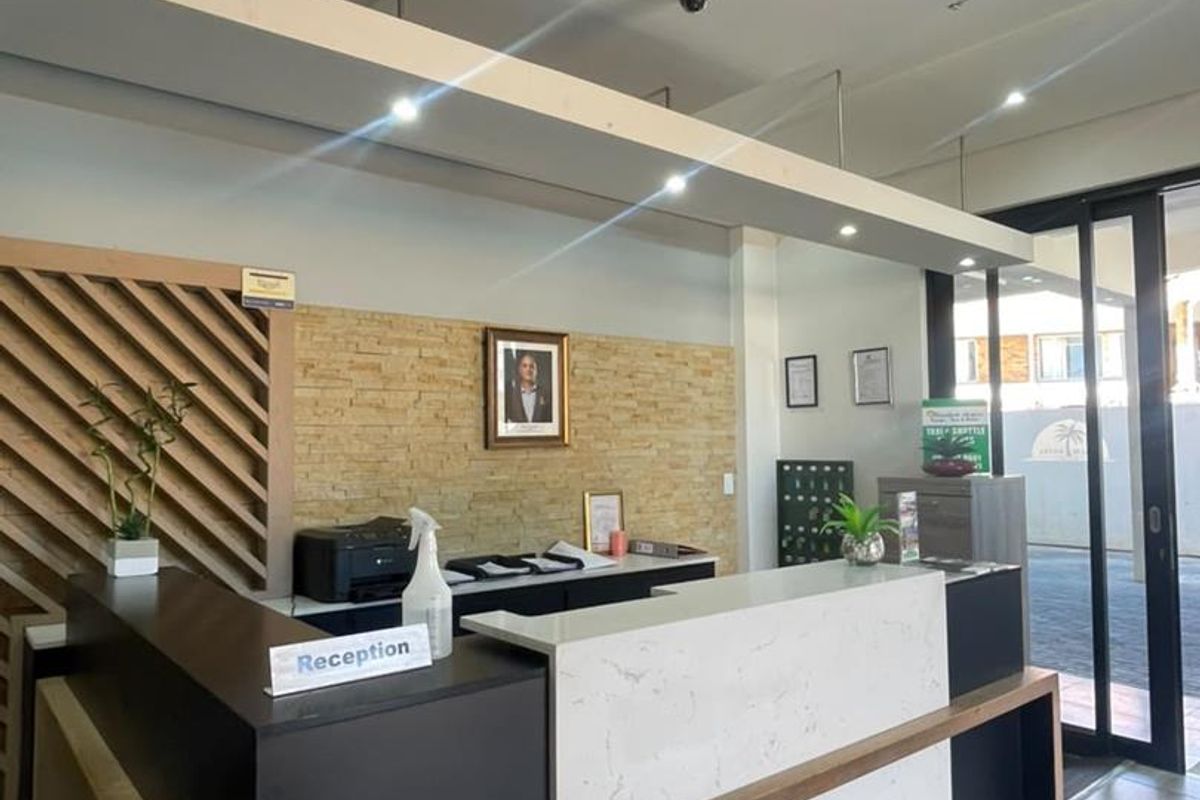 A professional reception area featuring a modern built-in desk, stone accent wall, ceiling-mounted air conditioning, and tiled flooring with glass entry doors.