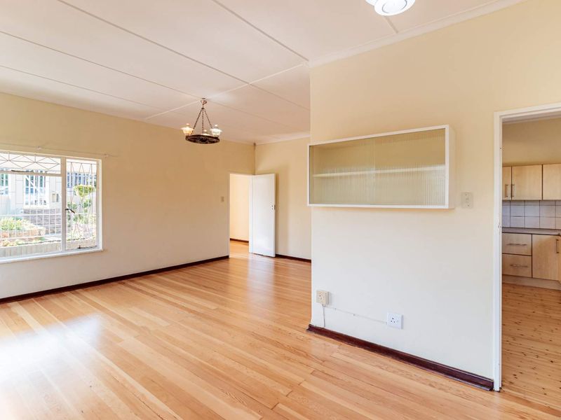 Spacious, light-filled living area featuring polished hardwood flooring, a built-in wall cabinet, and direct access to the adjacent kitchen.