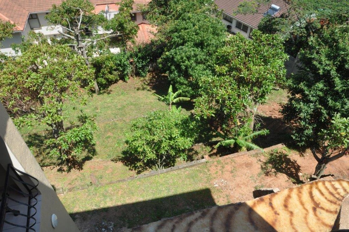 An elevated view overlooking a private garden area with established trees and lawn, viewed from an upper-level apartment balcony.