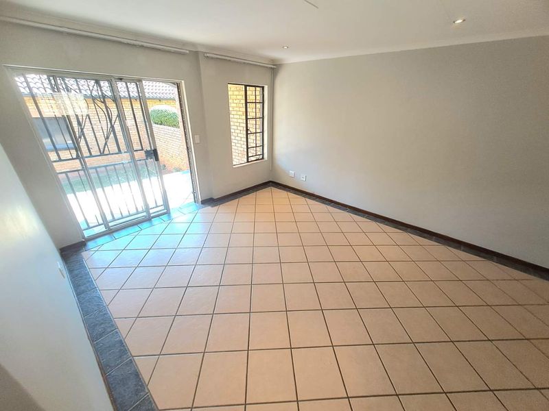 An empty, tiled living room featuring recessed lighting and a sliding glass door with a security gate leading to the exterior.