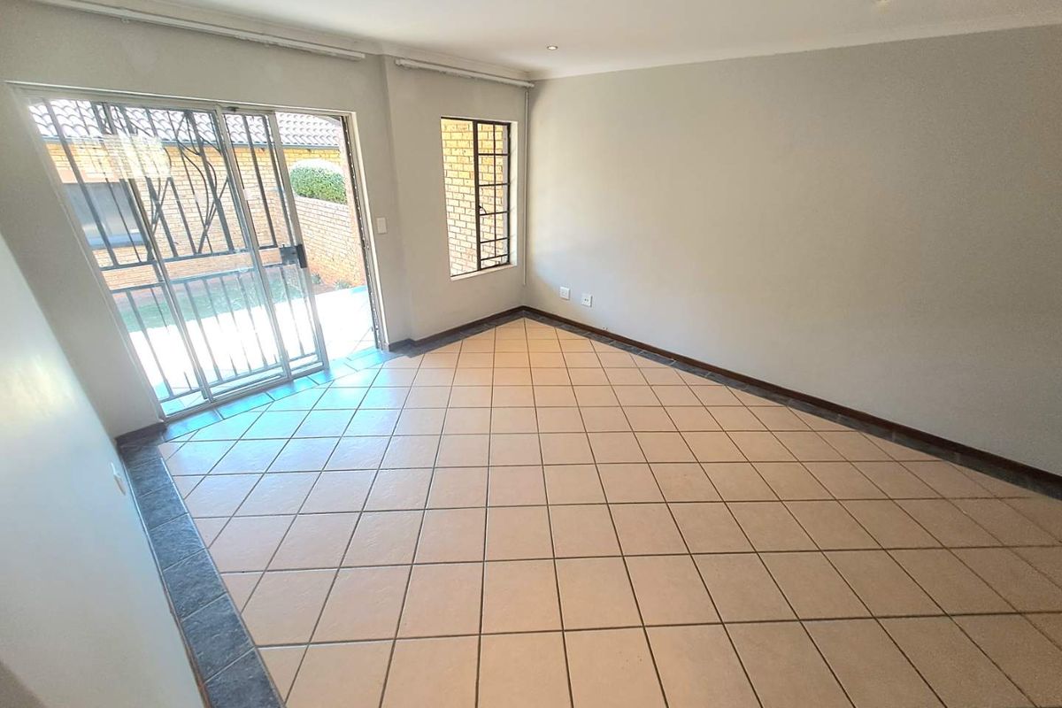 An empty, tiled living room featuring recessed lighting and a sliding glass door with a security gate leading to the exterior.