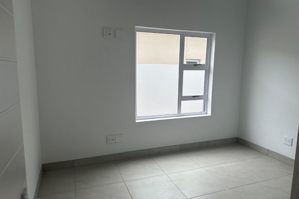 A clean, empty bedroom featuring neutral floor tiles, white walls, and a modern window with privacy glass.