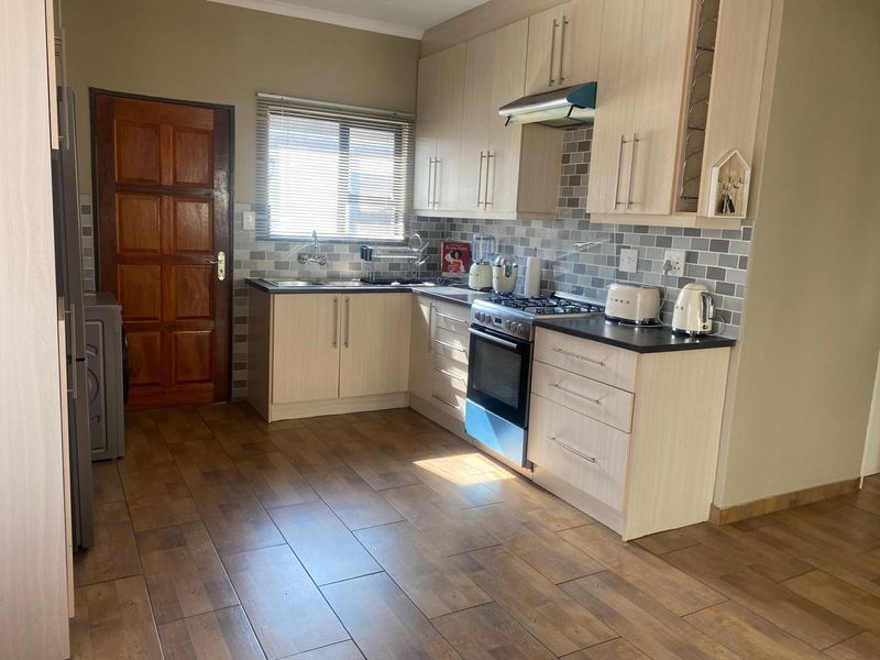 A functional kitchen featuring light wood-tone cabinetry, dark countertops, a gas stove with extractor fan, and modern wood-look floor tiles.
