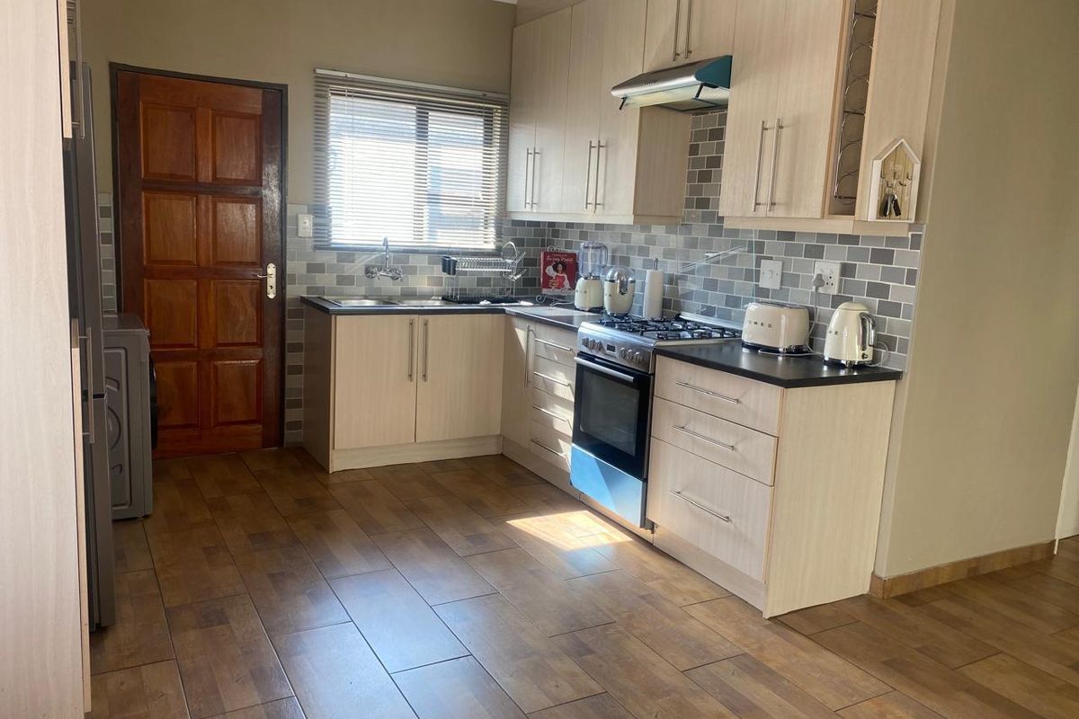 A functional kitchen featuring light wood-tone cabinetry, dark countertops, a gas stove with extractor fan, and modern wood-look floor tiles.