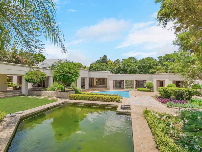 Spacious rear garden featuring a swimming pool, a large koi pond, paved patio areas, and a covered veranda overlooking the landscaped grounds.