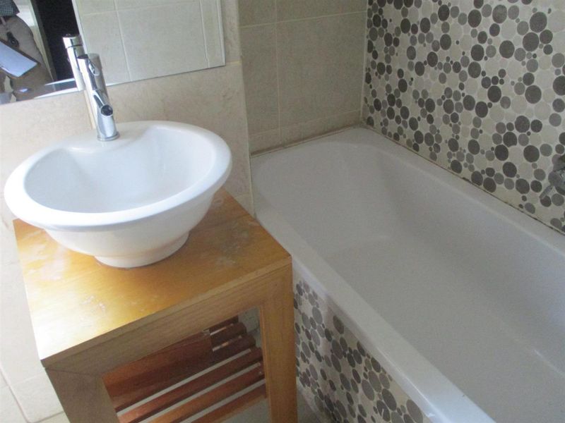 A bathroom featuring a vessel sink with chrome faucet and a built-in bathtub accented with decorative mosaic tiling.