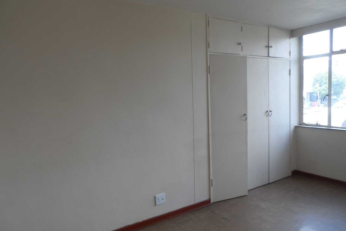 An empty bedroom featuring built-in cupboards, metal-framed windows, and basic flooring, offering a blank canvas for renovation or staging.