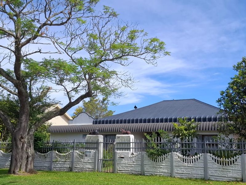 Front elevation of a residential property featuring a metal roof, secure precast concrete fencing, and a gated entrance with mature landscaping.