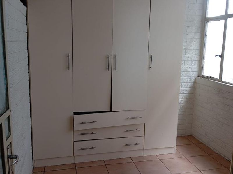 A bedroom featuring tiled flooring, painted brick walls, and a built-in wardrobe with visible wear and misalignment.