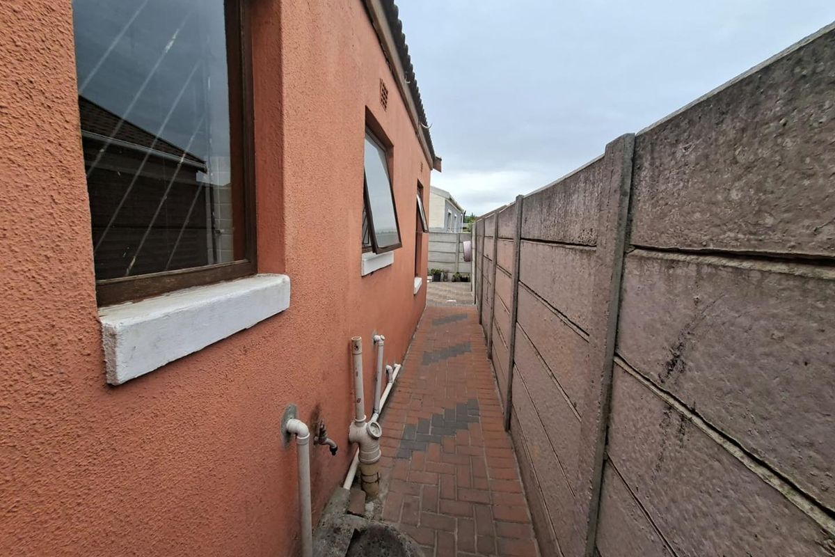 A narrow side passage of the townhouse featuring paved flooring, exterior wall access, and a precast concrete boundary wall.