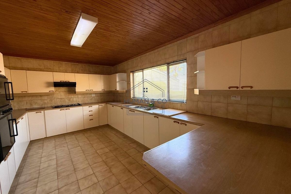 Spacious kitchen featuring extensive cabinetry, built-in oven, hob, extractor fan, and tiled flooring with a timber-paneled ceiling.