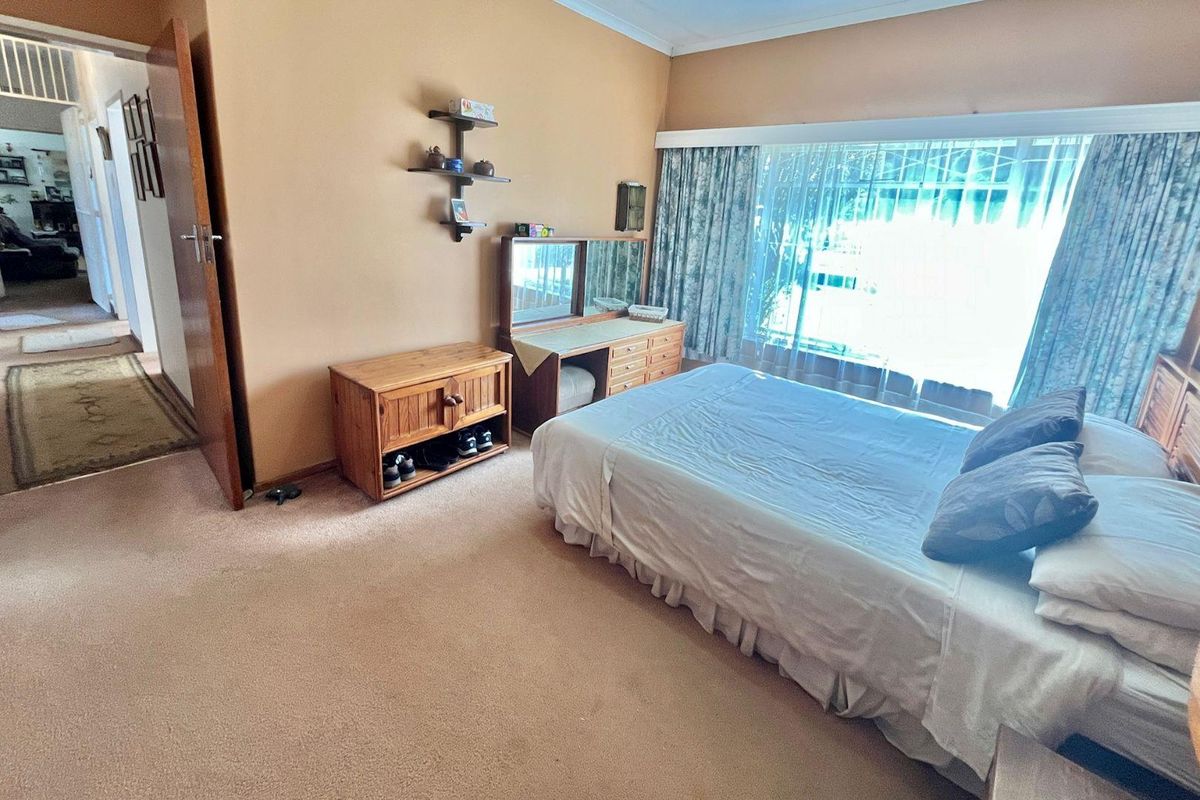 A spacious bedroom featuring neutral wall tones, carpeted flooring, and a large window with curtains, providing a comfortable and functional living space.