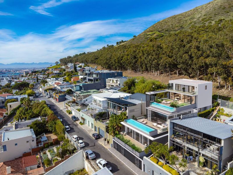 Aerial view of a modern multi-level apartment complex featuring rooftop swimming pools, expansive balconies, and contemporary architectural design in a hillside setting.