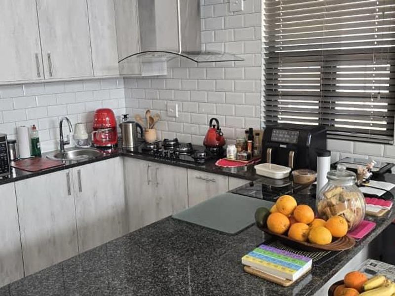Modern kitchen featuring granite countertops, subway tile backsplash, stainless steel extractor fan, gas hob, and light wood-look cabinetry.