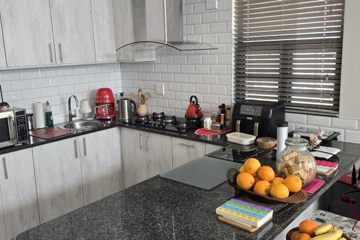 Modern kitchen featuring granite countertops, subway tile backsplash, stainless steel extractor fan, gas hob, and light wood-look cabinetry.