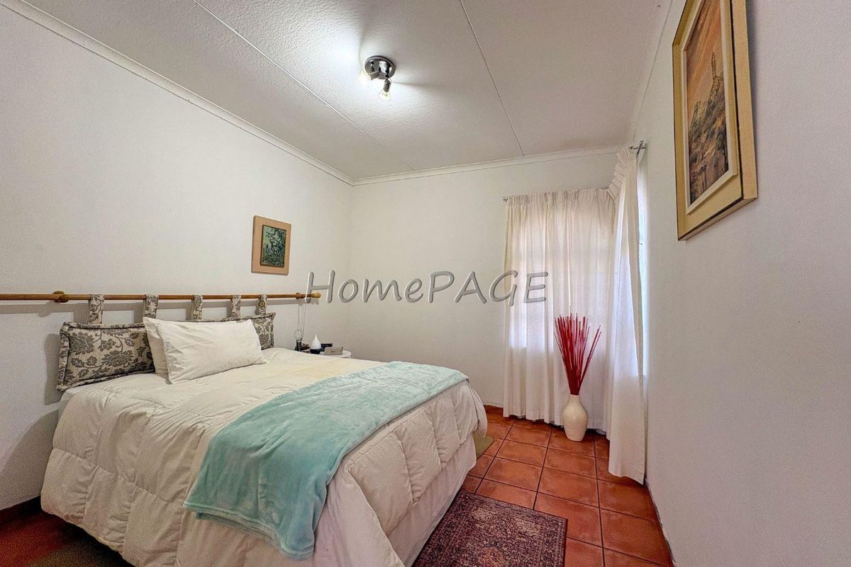 A standard bedroom featuring terracotta floor tiles, white walls, and a ceiling-mounted light fixture.