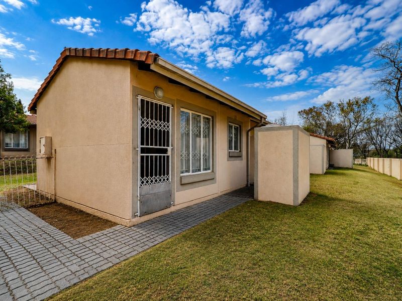Rear view of the cluster property featuring a paved walkway, well-maintained lawn, and secure access point with a security gate.
