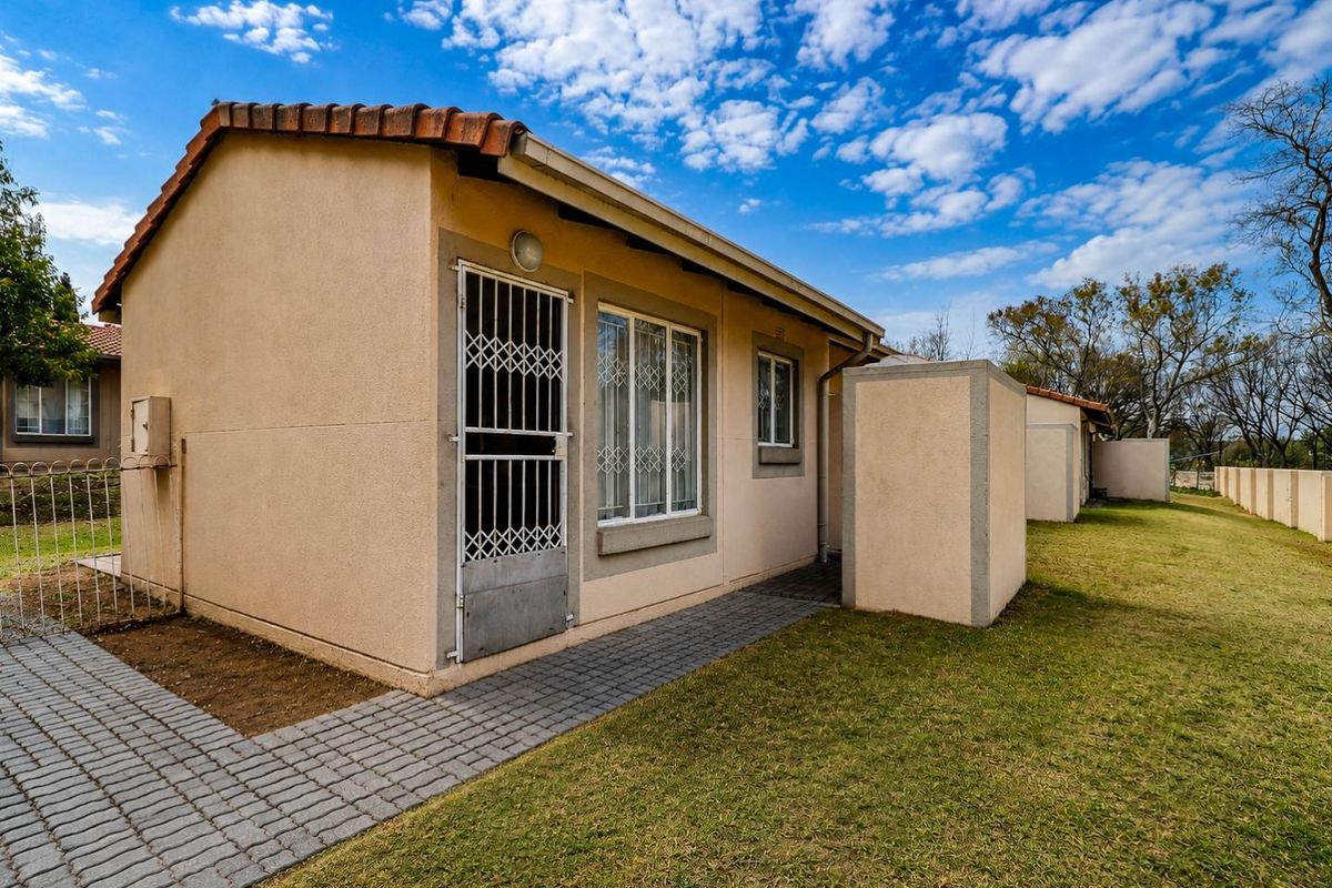 Rear view of the cluster property featuring a paved walkway, well-maintained lawn, and secure access point with a security gate.