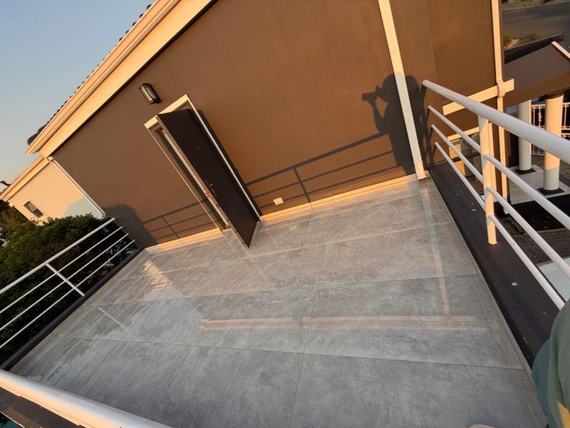 A spacious, tiled balcony area featuring a modern metal balustrade and direct access to the building interior.