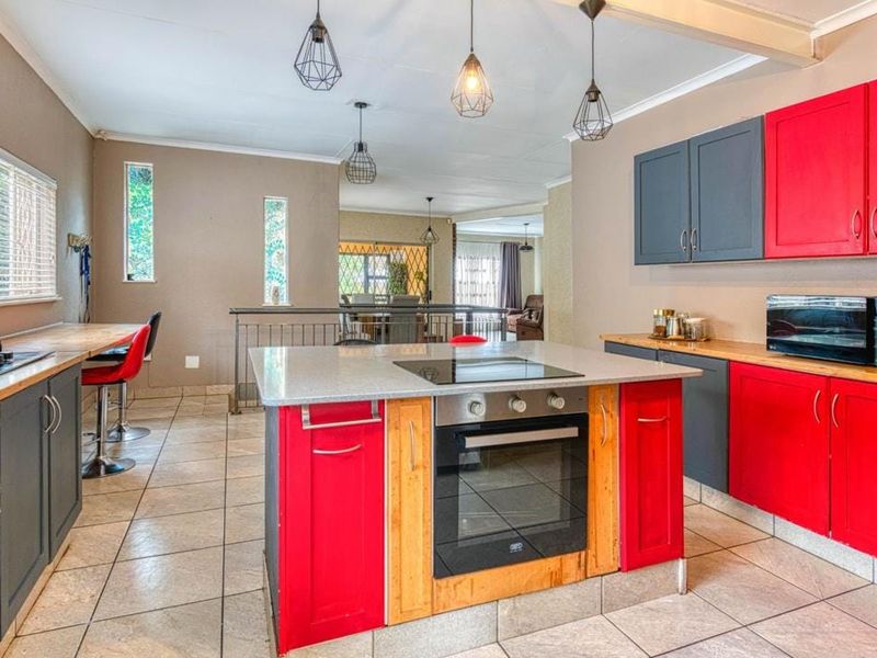 Spacious kitchen featuring a central island with built-in oven and cooktop, contrasting cabinetry, and tiled flooring, opening into an adjacent living area.