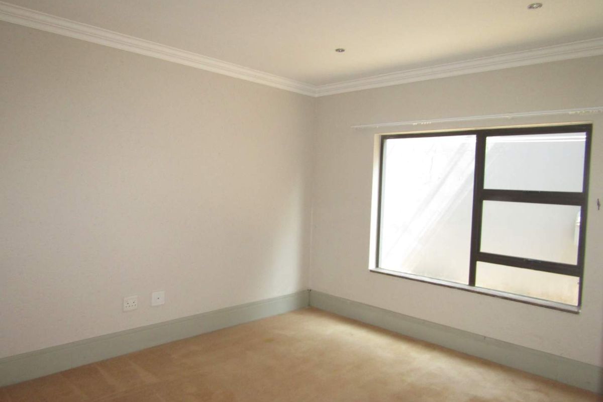 A clean, empty bedroom featuring neutral walls, crown molding, carpeted flooring, and a large window with dark frames.