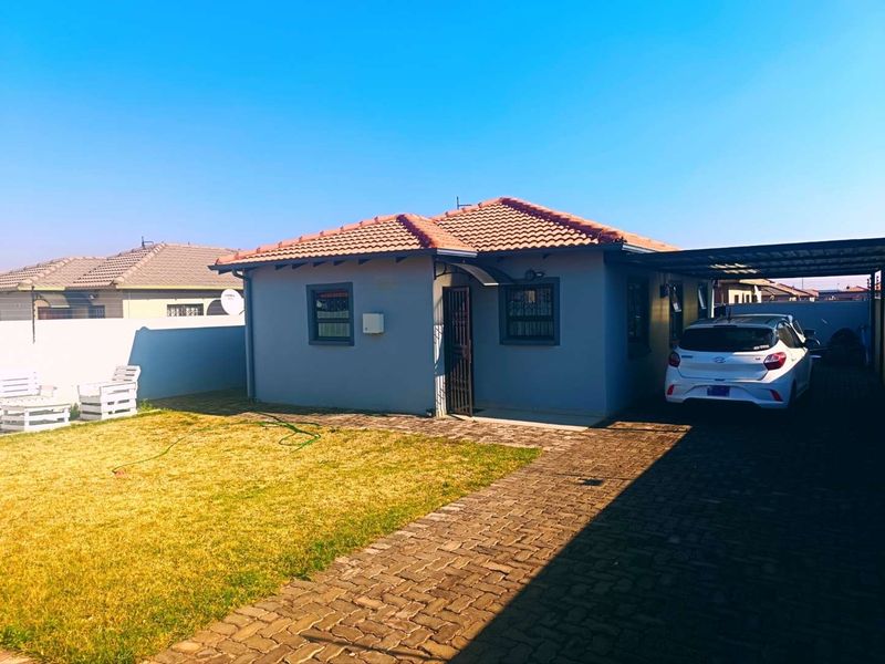 A well-maintained single-story house featuring a tiled roof, paved driveway, carport, and secure boundary wall in a residential setting.