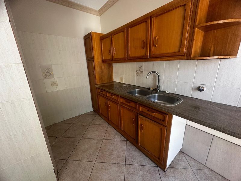 A functional scullery area featuring wooden cabinetry, granite countertops, a double stainless steel sink, and tiled finishes throughout.