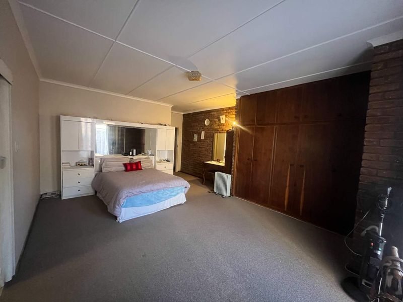 Spacious bedroom featuring extensive built-in wooden cupboards, an exposed brick feature wall, and neutral carpeting.