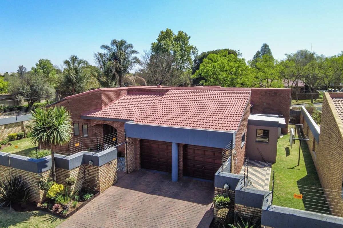 Aerial view of a brick-faced residential property featuring a double garage, tiled roof, and landscaped garden area.