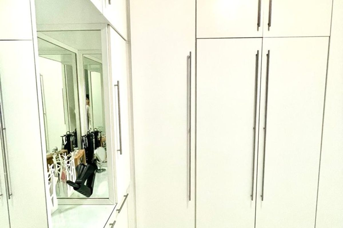 A modern bedroom featuring extensive white built-in cabinetry, a dedicated vanity area with a large mirror, and clean tiled flooring.