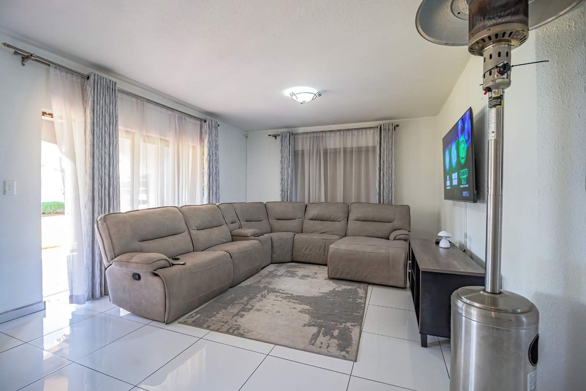 A bright and spacious living room featuring large sliding glass doors, neutral tiled flooring, and modern curtain fixtures.