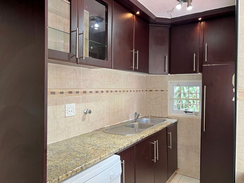 A functional scullery featuring dark wood cabinetry, granite countertops, a double basin sink, and tiled backsplash with integrated lighting.