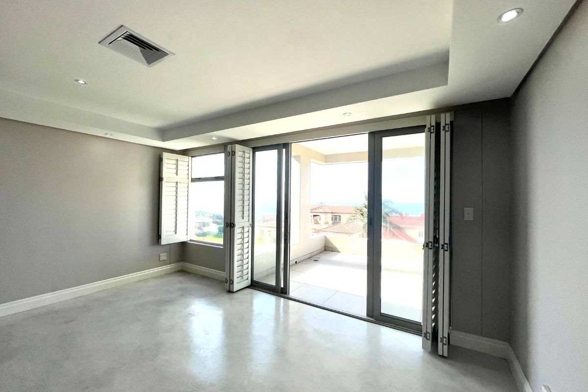 A bright, modern living area featuring polished concrete floors, recessed ceiling lighting, and large bi-fold doors opening onto a private balcony with scenic views.