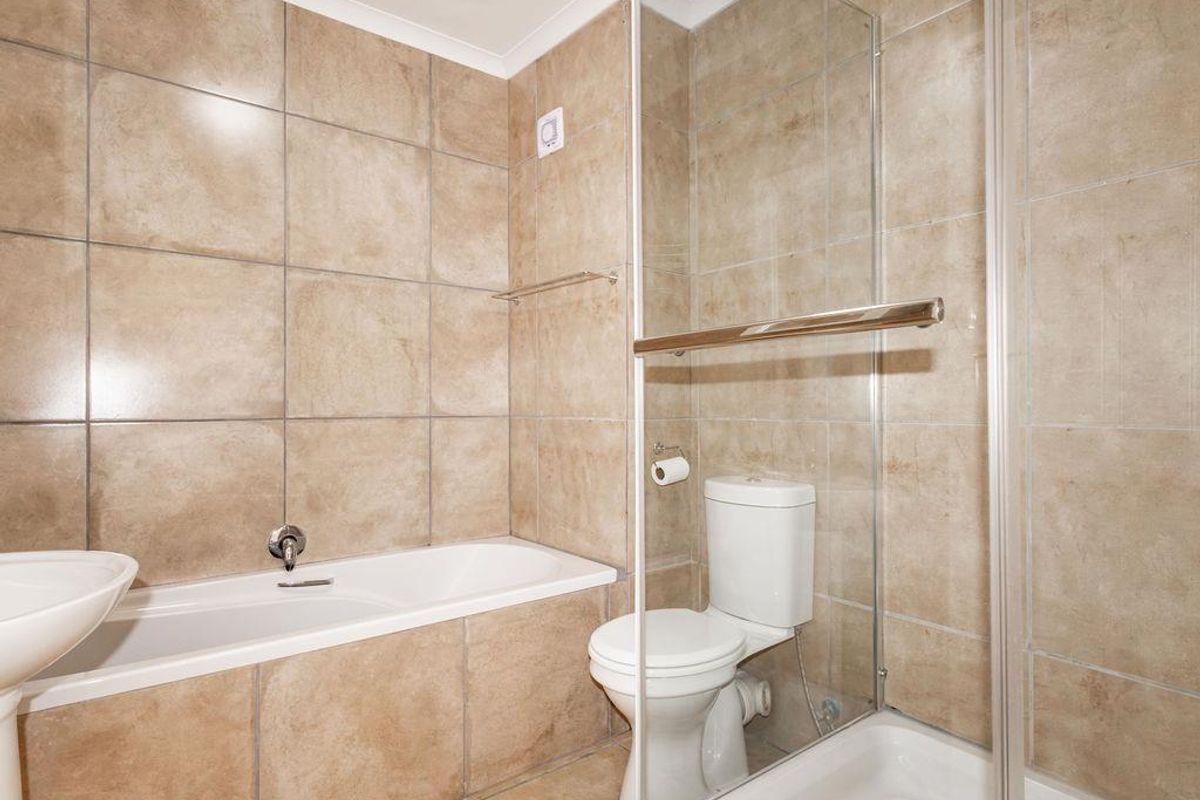 A functional bathroom featuring a bathtub, separate shower enclosure, toilet, and pedestal sink with neutral wall and floor tiling.