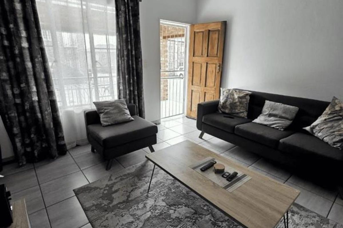 A living room featuring tiled flooring, a panelled ceiling, and a timber entrance door, providing access to the exterior.