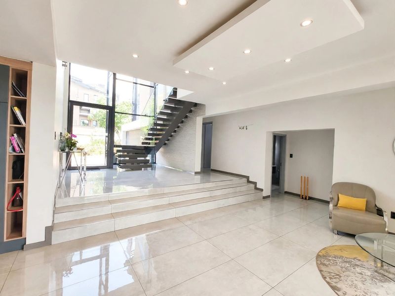 Spacious modern entrance hall featuring a striking floating staircase, large glass entrance door, polished tiled flooring, and integrated ceiling lighting.
