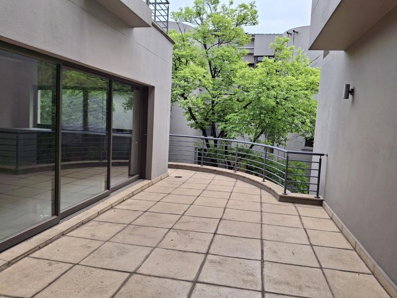 A spacious, empty balcony featuring tiled flooring, a metal safety balustrade, and large sliding glass doors providing access to the interior.