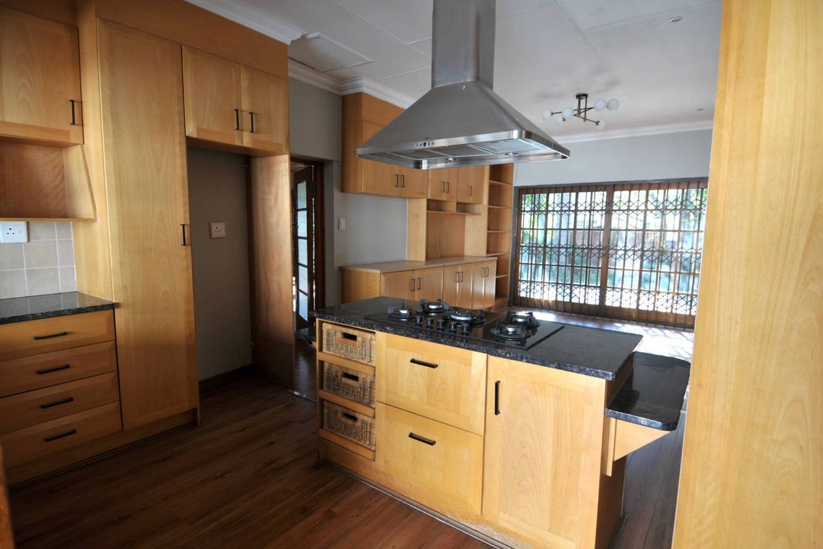 A functional kitchen featuring light wood cabinetry, a central island with a built-in gas hob, stainless steel extractor fan, and dark stone countertops.