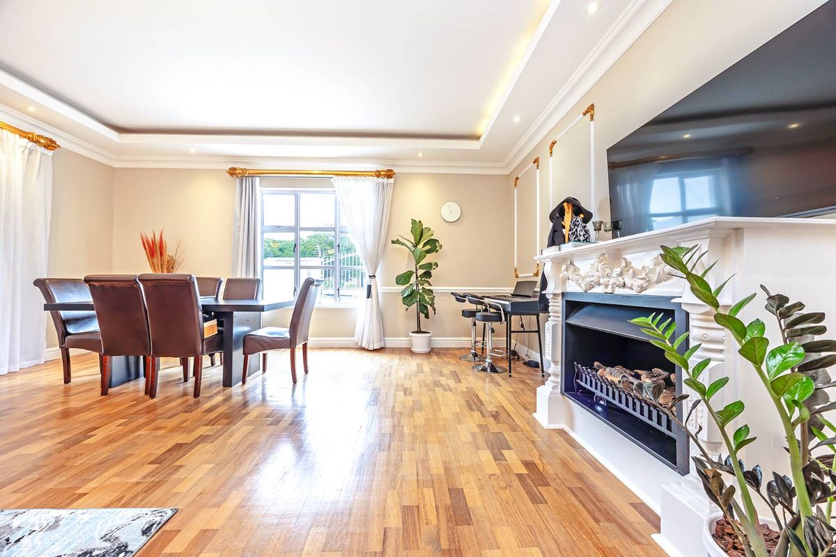 Spacious living room featuring hardwood flooring, decorative wainscoting, recessed ceiling lighting, and a classic fireplace with a detailed mantelpiece.