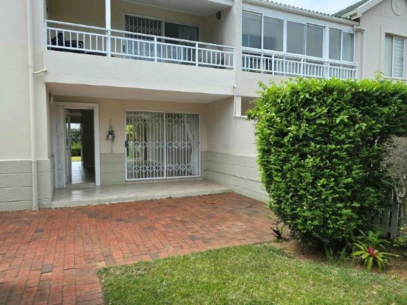 Rear view of the townhouse featuring a brick-paved patio, a small garden, and an upper-level balcony with security railings.