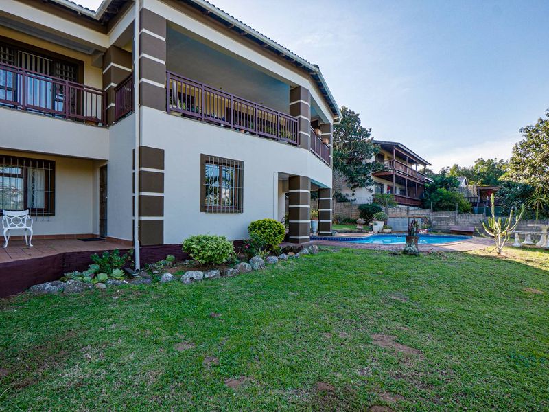 Rear view of the multi-story house featuring a covered patio, balcony with railings, swimming pool, and landscaped garden area.