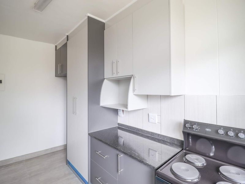 A clean, modern kitchen featuring grey and white built-in cabinetry, granite countertops, a tiled backsplash, and a freestanding electric stove.