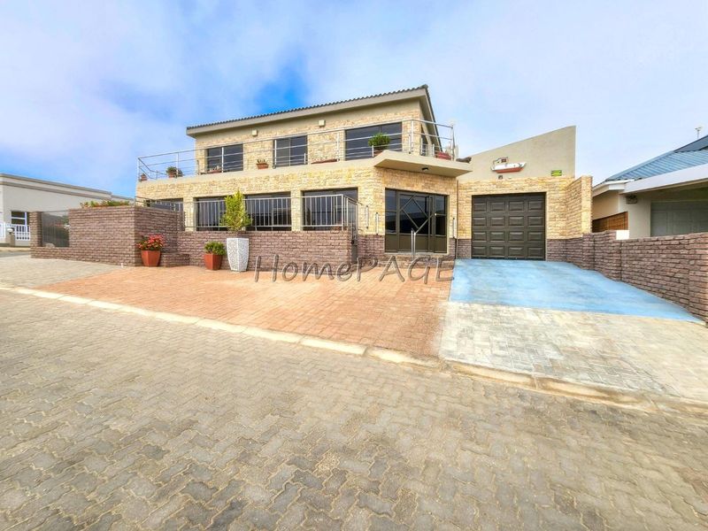 Front elevation of a multi-level house featuring stone cladding, a paved driveway, a single garage, and an upper-level balcony with metal railings.
