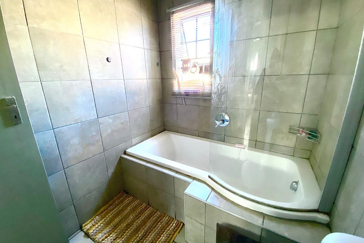 A functional bathroom featuring a built-in bathtub with a glass shower screen, tiled walls, and a window for natural light.