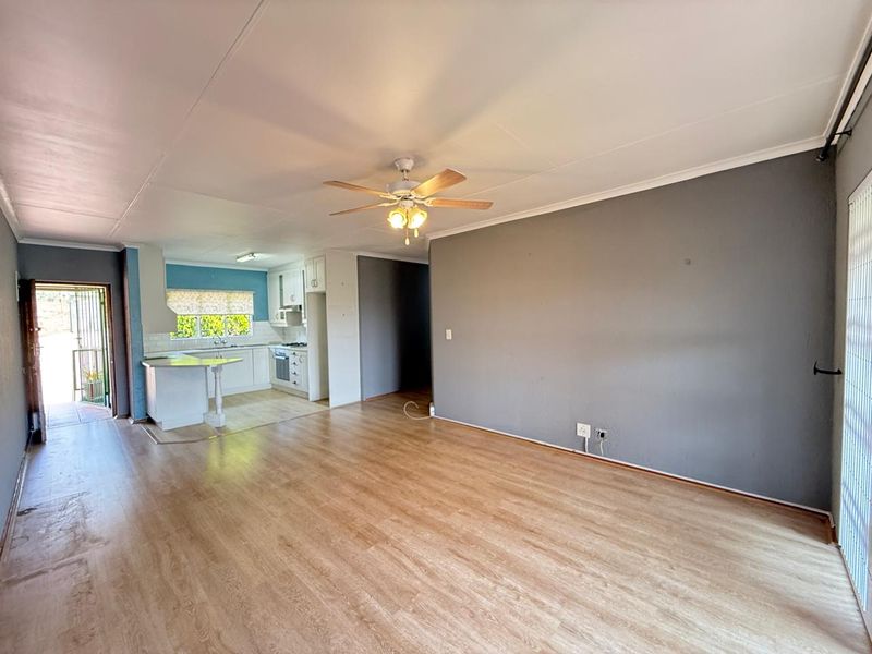 Spacious open-plan living area featuring laminate flooring, a ceiling fan, and an adjoining kitchen with built-in cabinetry and appliances.