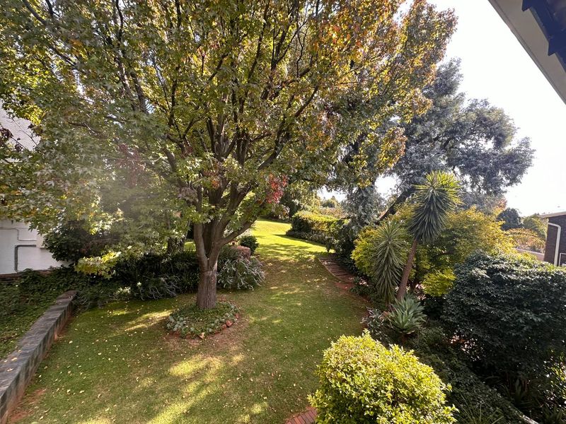 A well-maintained, lush garden area featuring mature trees, established landscaping, and a stone retaining wall, providing a peaceful outdoor setting.